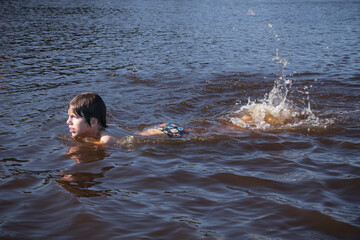 Boy swimming with splashes in blue water of river, sea or lake.