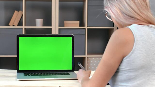Back view female student making paper notes during elearning online education laptop green screen