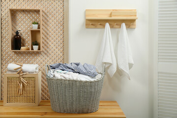 Wicker basket with dirty laundry on wooden table in bathroom