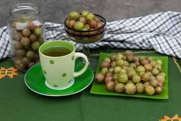 Still life in shades of green. There are gooseberries, a green cup with a drink 