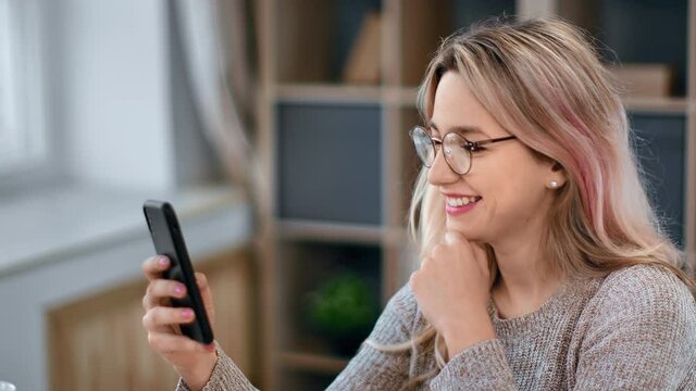 Closeup happy hipster female in glasses chatting surfing internet use smartphone at home office