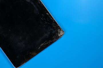 Tablet computer with broken screen glass, the result of falling or crash. Vibrant blue background, copy space.