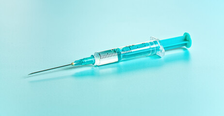 Cyan coloured injection syringe and needle with clear liquid on a board, close-up detail