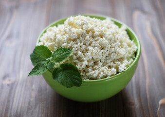 Cottage cheese with mint in a green bowl on a wooden table.