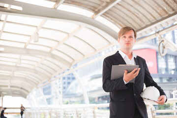 A handsome man is standing with a clipboard and an engineer's hat in the corridor.