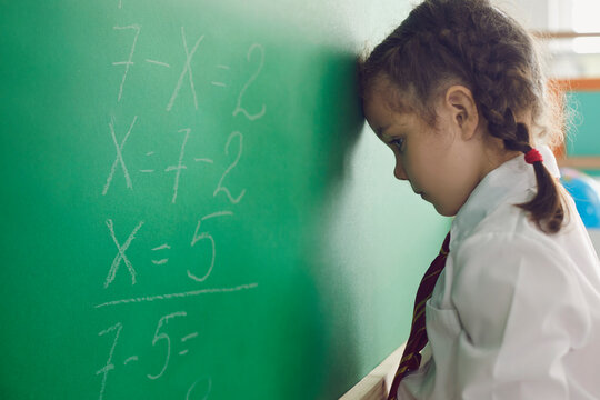 Back to school. Little schoolgirl has a problem with a math problem on a school board in the classroom. Upset child thinks in class
