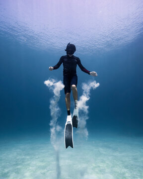 Person freediving in the ocean, playing with sand