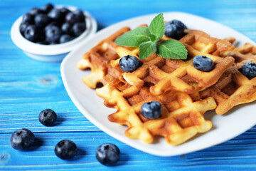 Traditional belgian waffles with fresh berrys and sugar powder on white plate, blue wooden background.