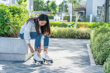 Asian girl tying her roller skates on a roller skating park in the park 