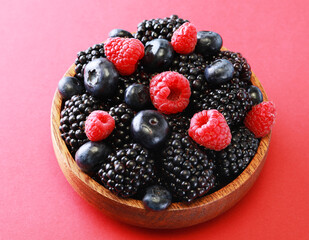 Fresh berries salad in a wooden plate on red background.