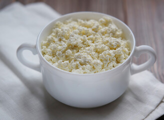 Cottage cheese in a white bowl on a white napkin. Top view.