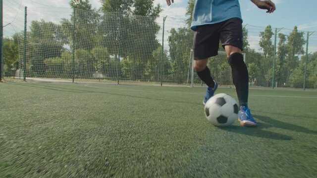 Close-up front view of soccer player legs in football boots and sportswear, dribbling, demonstrating close ball control, quick feet, performing football tricks and moves on football pitch at daybreak