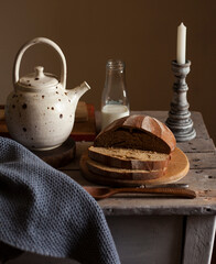 Freshly baked sliced rye bread on wooden cutting board,teapot with tea,bottle of milk and candlestick. flat lay