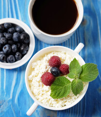 Cottage cheese with fresh berries and coffee on a blue wooden background. Close up.