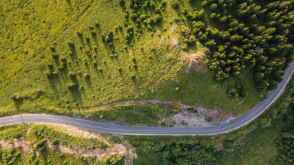 Aerial view of countryside road passing through the green forest and mountain. Aerial view over mountain road going through forest landscape.