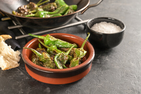 Fried peppers de padron or green pimientos in a traditional Spanish tapa bowl on a dark gray slate background, copy space, selected focus