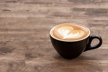 Black coffee cup of art latte with froth heart shaped  on wooden table. copy space for text design.