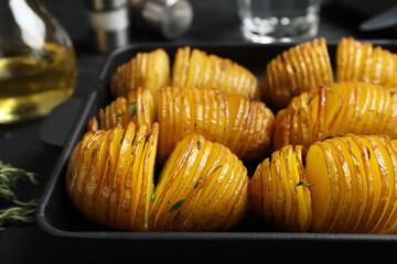 Delicious homemade Hasselback potatoes in baking pan on black table, closeup