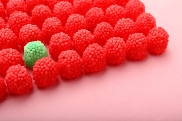 Delicious green gummy raspberry candy among red ones on pink background