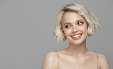 Portrait of a beautiful smiling blonde girl with a short haircut. Gray background.