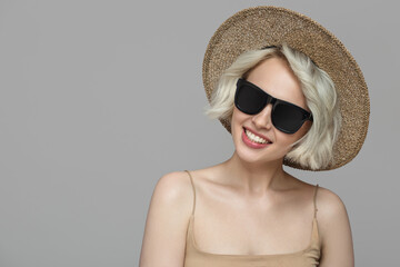 Fototapeta premium Smiling girl with a short haircut in a hat and sunglasses. Grey background.