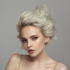 Portrait of a beautiful blonde girl with a short haircut. Gray background.