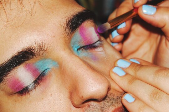 closeup portrait of queer young man getting trans pride flag eye makeup / eyeshadow in pink blue & white colors