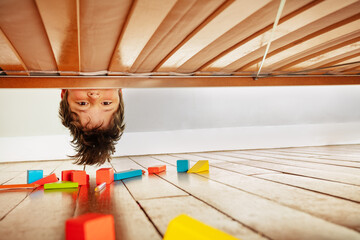 Funny portrait of a boy look down under the bed