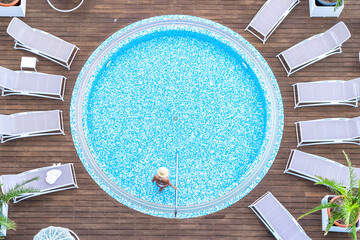Young alone beautiful sports woman in bikini and hat is swimming in hydro massage bath on wooden...