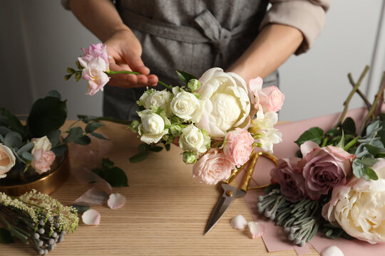 Florist creating beautiful bouquet at wooden table indoors, closeup
