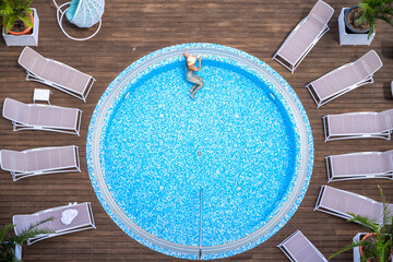 Young alone beautiful sports woman in bikini and hat is swimming in hydro massage bath on wooden...