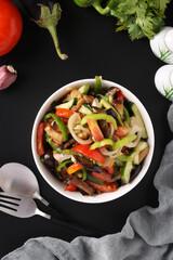 Salad with eggplants, tomatoes, peppers and cucumbers in white bowl on black background, Top view
