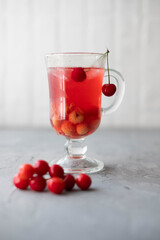 Fresh cherry fruit juice compote in a glass with ice on a light background