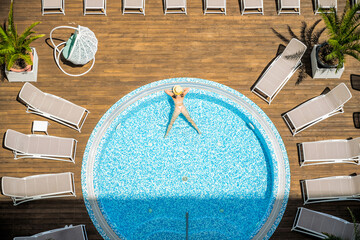 Young alone beautiful sports woman in bikini and hat is swimming in hydro massage bath on wooden...