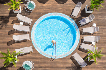 Young alone beautiful sports woman in bikini and hat is swimming in hydro massage bath on wooden terrace. Aerial drone view. Tropical summer luxury hotel
