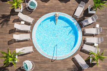 Young alone beautiful sports woman in bikini and hat is swimming in hydro massage bath on wooden...