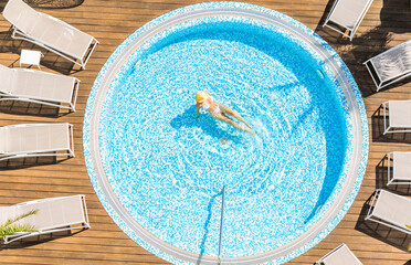 Young alone beautiful sports woman in bikini and hat is swimming in hydro massage bath on wooden...