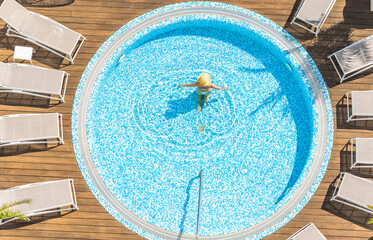 Young alone beautiful sports woman in bikini and hat is swimming in hydro massage bath on wooden...
