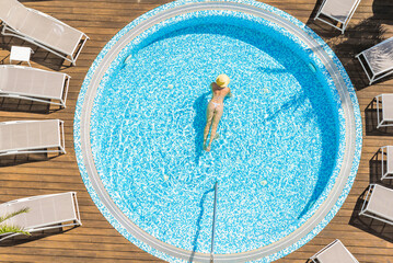 Young alone beautiful sports woman in bikini and hat is swimming in hydro massage bath on wooden...