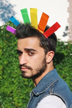 Portrait of queer young man wearing a fun hat of lgbtq rainbow pride flag hat 