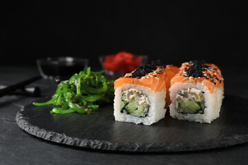 Delicious sushi rolls and chuka on black slate table