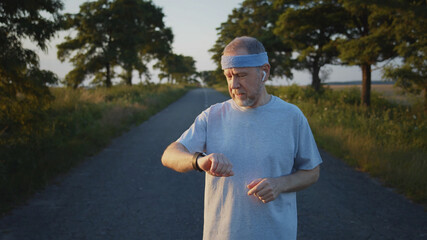 Mature caucasian blonde bearded man using smartwatch outside running training sport. Healthy lifestyle. Athletic male person checking app notification online. Navigation app, Hologram picture.