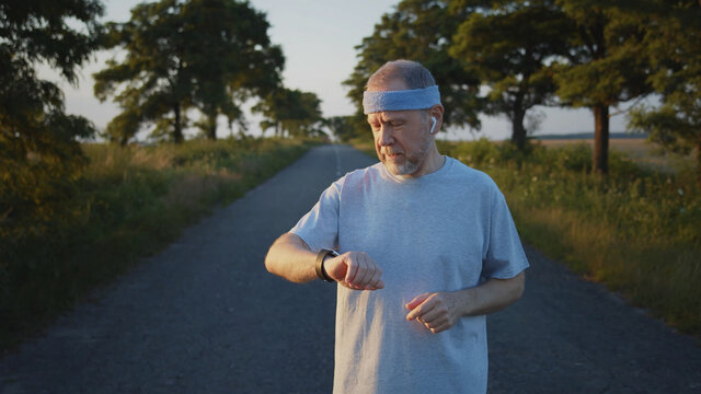 Mature caucasian blonde bearded man using smartwatch outside running training sport. Healthy lifestyle. Athletic male person checking app notification online. Navigation app, Hologram picture.