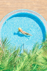 Young alone, beautiful sports woman in bikini and hat is swimming in swimming pool, hydro massage bath with palm trees. Aerial, above, drone view. Vertical ratio, size