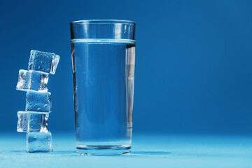 Ice cubes tower with a glass of cold and clean water on a blue background.