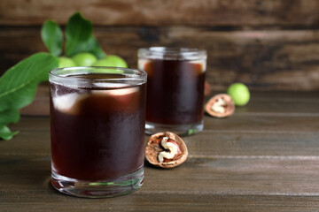 Delicious liqueur with ice and fresh walnuts on wooden table. Space for text