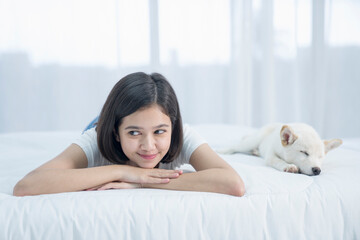 Pet Lover concept. Young Asian woman relaxing and playing with white shiba inu dogs on the bed in bedroom. Girl sleeping with Hokkaido inu on the bed.