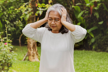 Elderly Asian woman, 60 years old, has headaches, severe dizziness, touches her head with her hands...