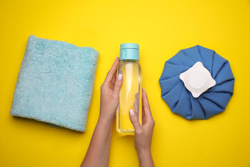 Woman with bottle of water, cold compress and towel on yellow background, top view. Heat stroke...
