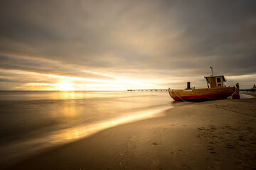 Obraz premium Fishing cutter on the Baltic Sea beach of Ahlbeck in the sun setting. Long exposure.